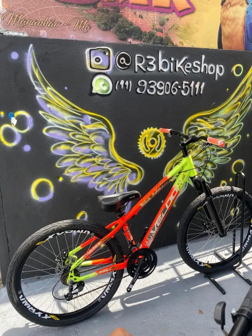 Bicicleta laranja e verde limão diante do mural de asas da R3 Bike Shop
