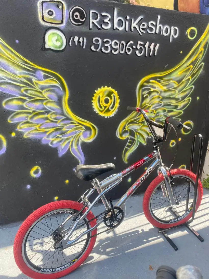 Bicicleta prata e vermelha diante do mural de asas da R3 Bike Shop