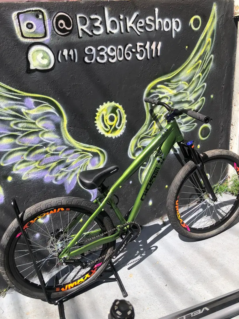 Bicicleta verde escura diante do mural de asas da R3 Bike Shop