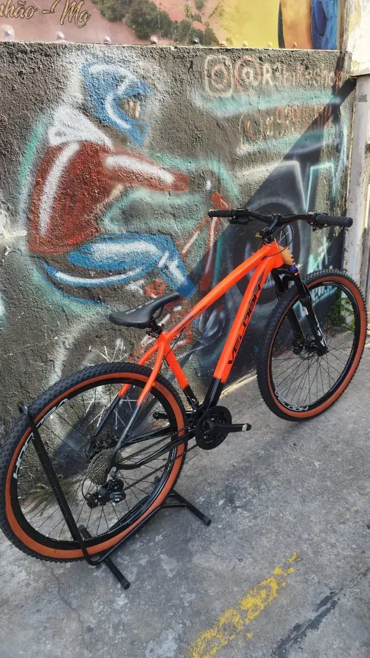 Bicicleta aro 29 laranja parada na calçada em frente à loja